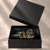کمربند چرمی مشکی با سگک فلزی طلایی به فرم لوگوی تایپی برند Chloé در حال معلق | Black leather belt with gold-tone metal cursive Chloé logo buckle, floating in mid-air