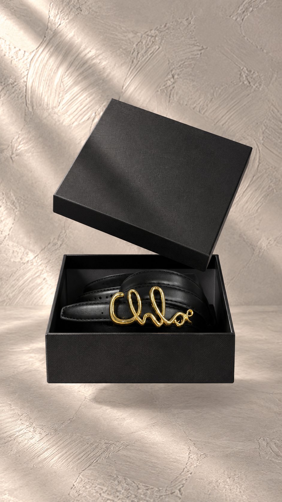 کمربند چرمی مشکی با سگک فلزی طلایی به فرم لوگوی تایپی برند Chloé در حال معلق | Black leather belt with gold-tone metal cursive Chloé logo buckle, floating in mid-air