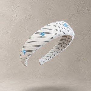 هدبند پهن پارچه‌ای سفید با خطوط راه‌راه مشکی و تزئینات مونوگرام آبی روی پس‌زمینه بژ