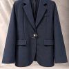 کت تک زنانه سرمه‌ای شیک با یقه انگلیسی و سگک فلزی مینیمال روی پس‌زمینه بتنی روشن | Tailored navy blue women’s blazer with modern metallic buckle closure floating against a minimal concrete background