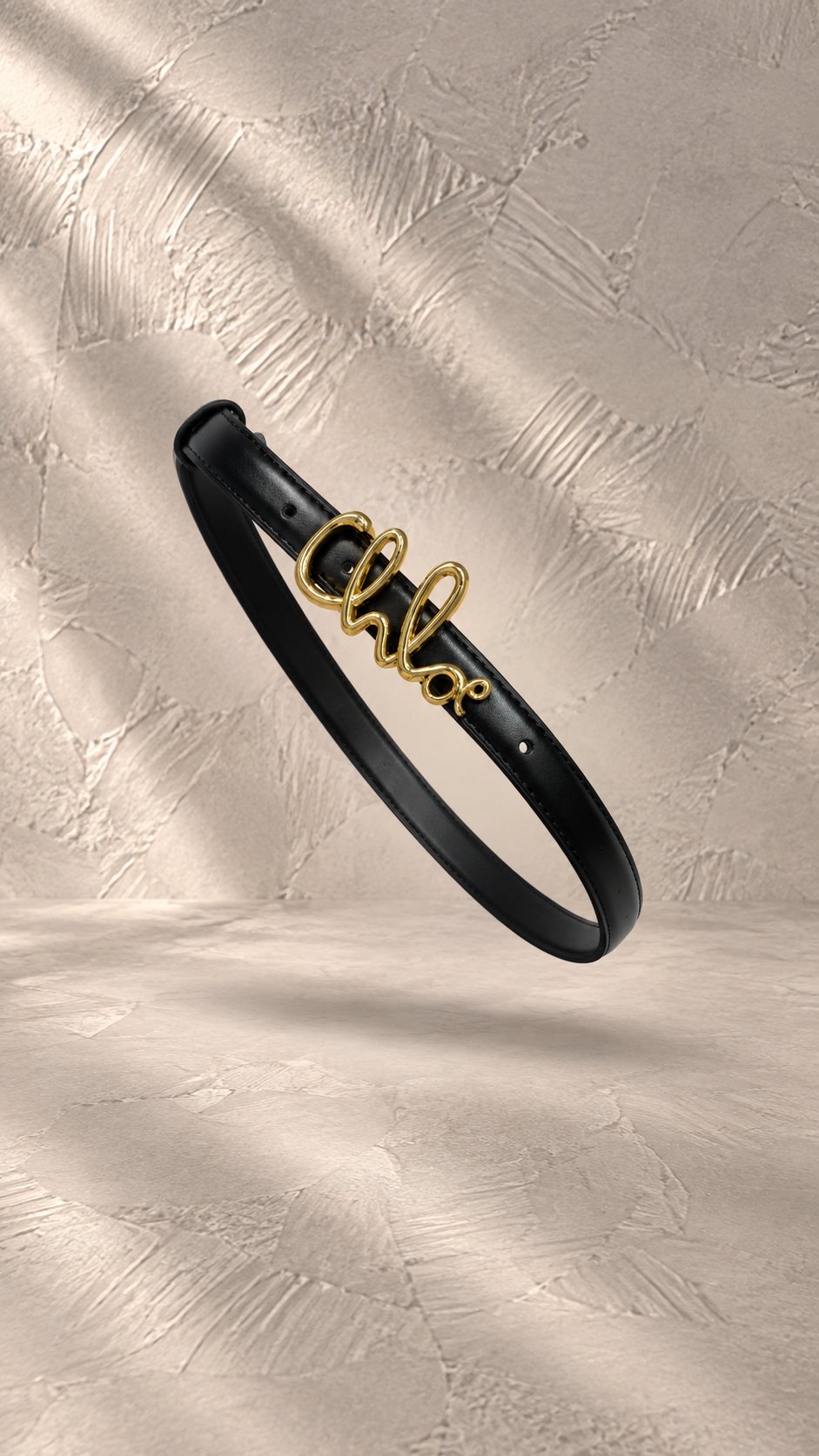 کمربند چرمی مشکی با سگک فلزی طلایی به فرم لوگوی تایپی برند Chloé در حال معلق | Black leather belt with gold-tone metal cursive Chloé logo buckle, floating in mid-air