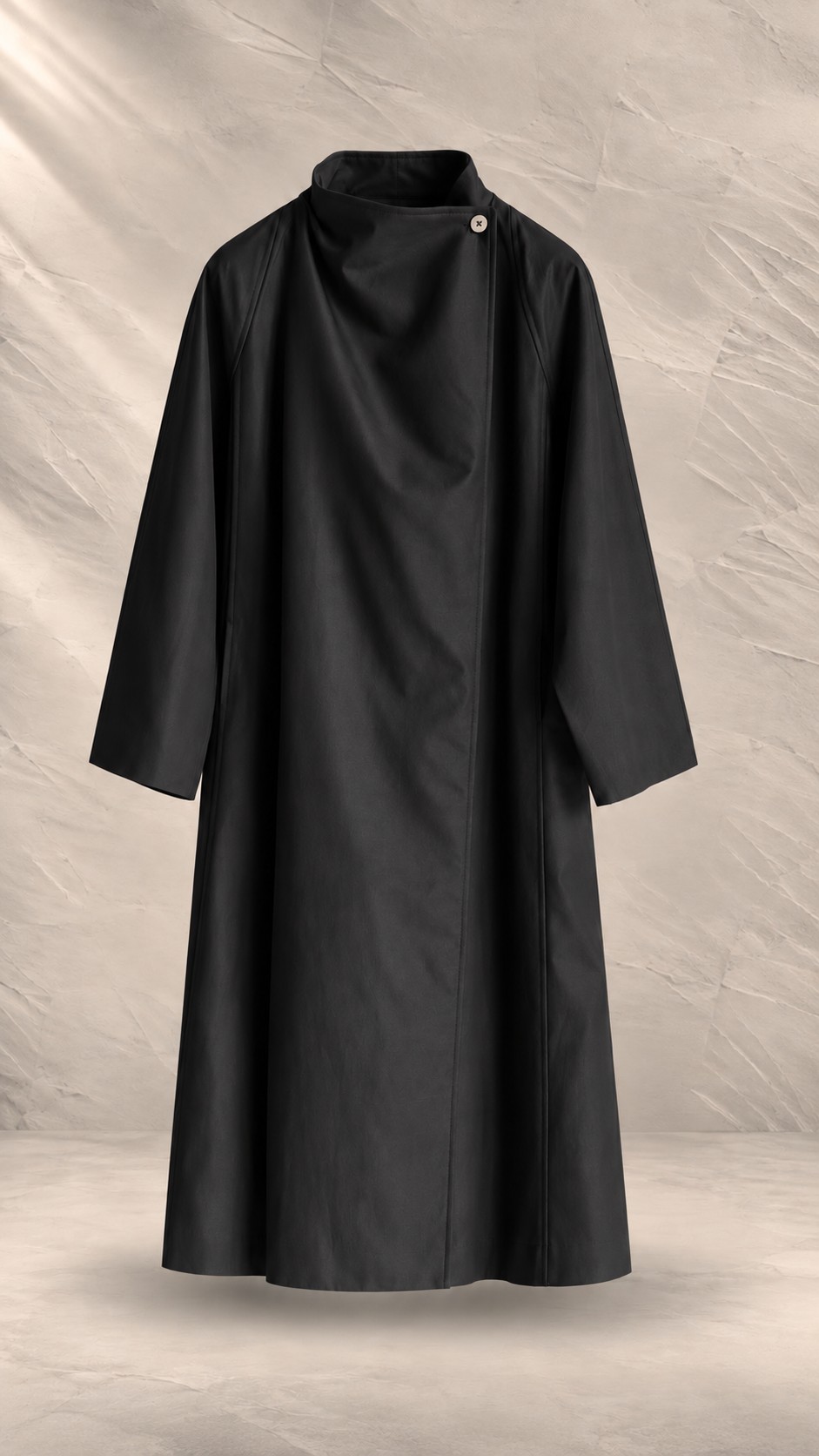 بارانی مینیمال با یقه دراپه مورب و تک‌دکمه چوبی شناور در پس‌زمینه بتنی بافت‌دار | Minimalist asymmetric drape trench coat with raglan sleeves and wooden accent button on textured neutral background