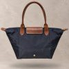 کیف دوشی تاشو زنانه لوشامپ از جنس نایلون با درپوش و بند چرمی با جزئیات یراق طلایی | Floating Longchamp Le Pliage foldable nylon tote bag with brown leather flap, handles, and gold-tone horse medallion zipper pull